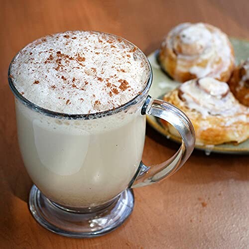 Glass mug of frothy cinnamon latte with pastries in the background.